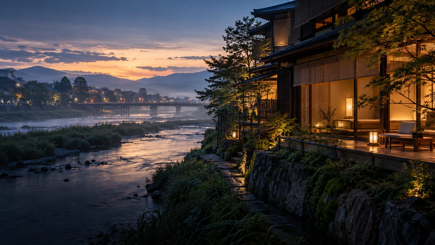 夕暮れの川辺に灯りのともる宿